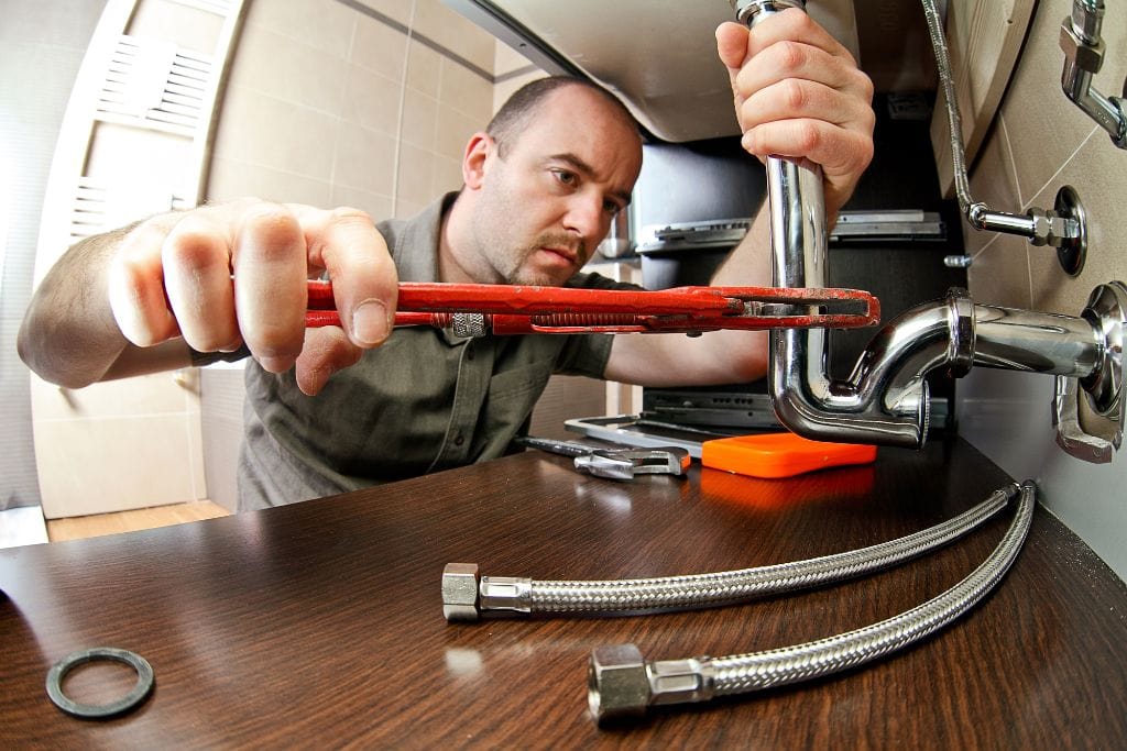 A plumber working on a sink with a wrench.
