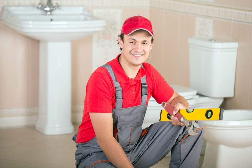 A plumber holding a measuring tool in front of a toilet.