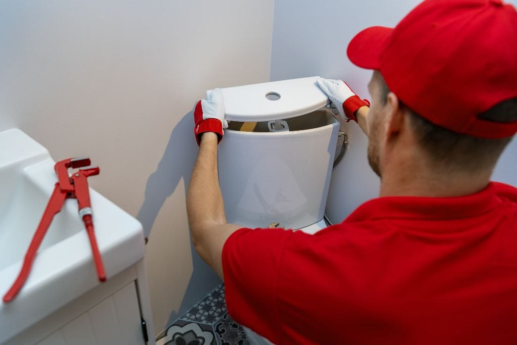 A plumber fixing a toilet in a bathroom.