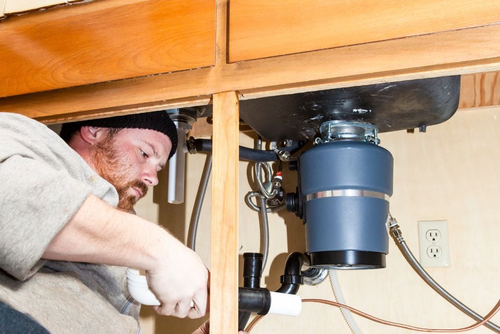 A man fixing a sink under a cabinet.