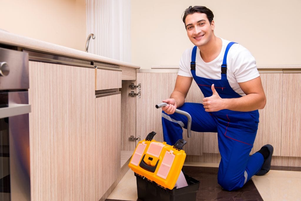 A man in overalls is kneeling down in front of a kitchen.