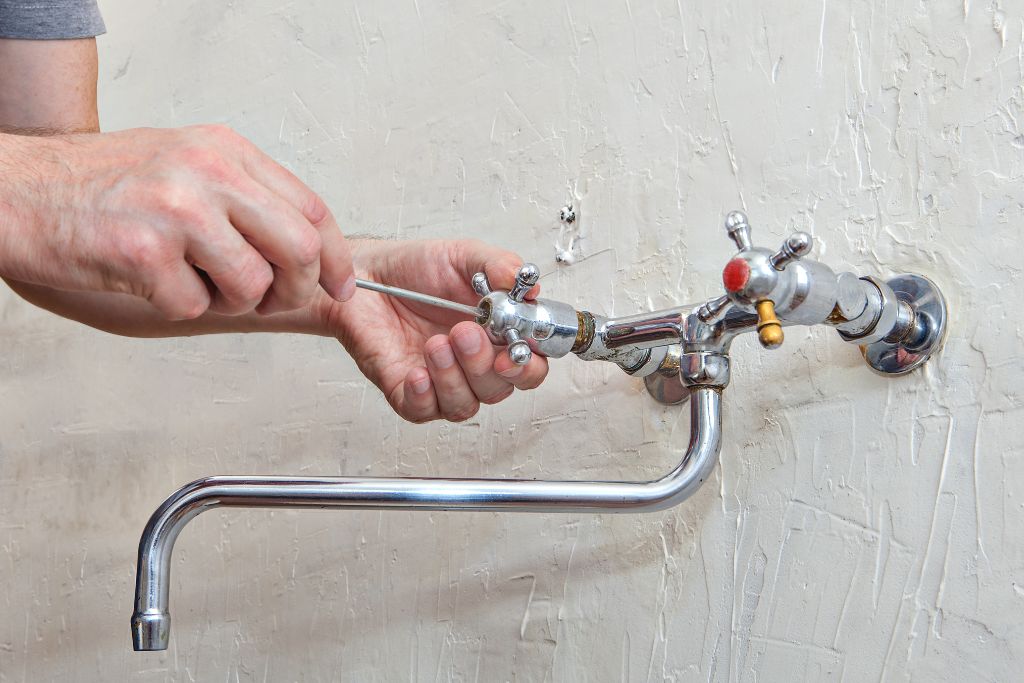 A man fixing a faucet on a wall.