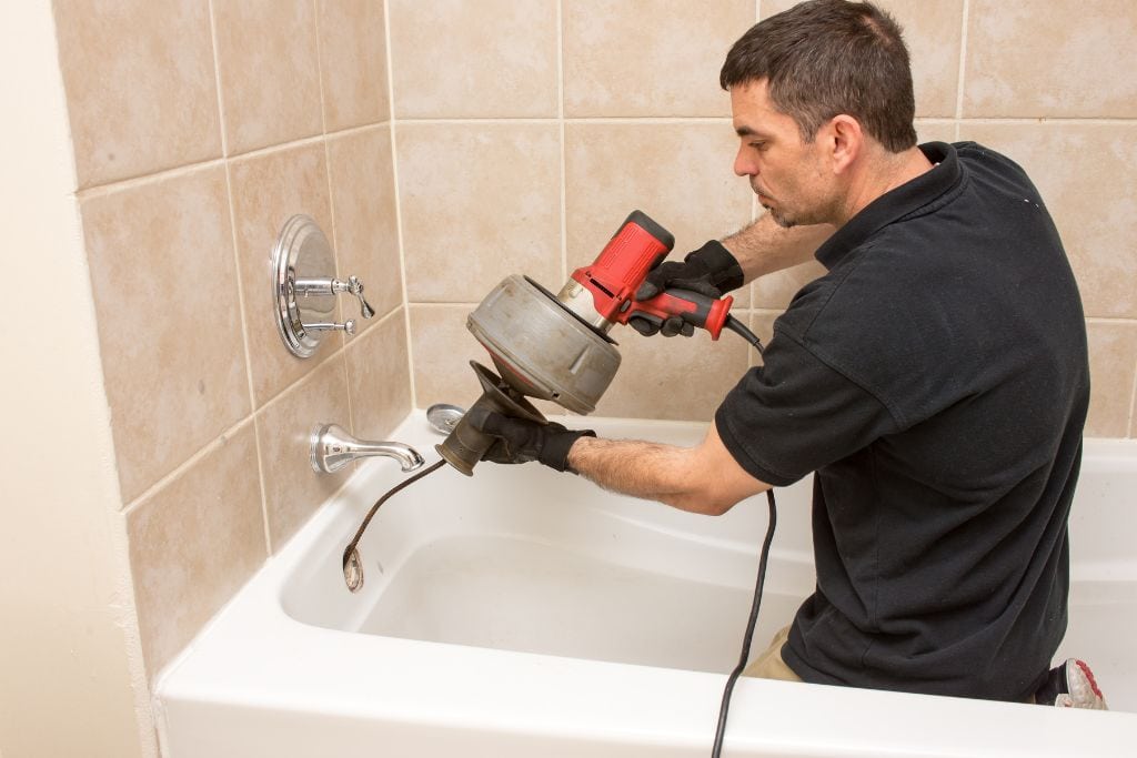 A man working on a bathtub with a drill.