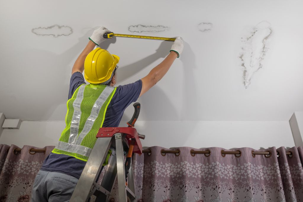 A construction worker repairing a ceiling with a ladder.