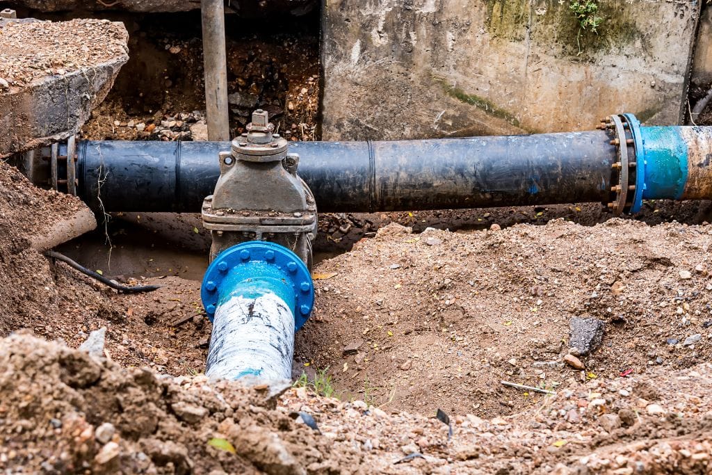 A water meter and pipes in a dirt area.