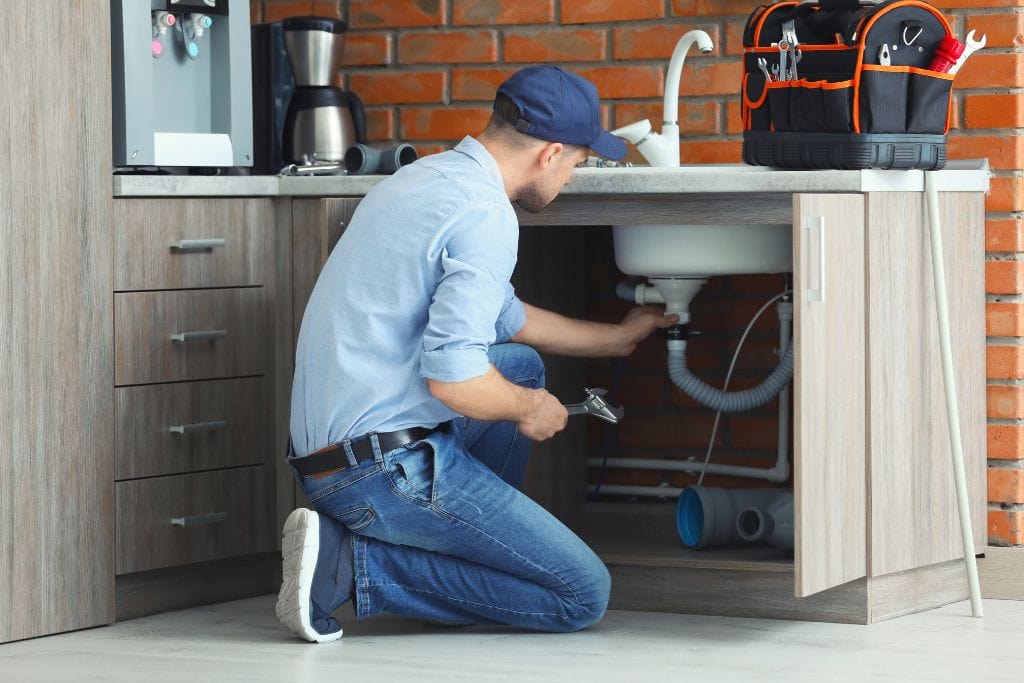 A plumber fixing a sink in a kitchen.
